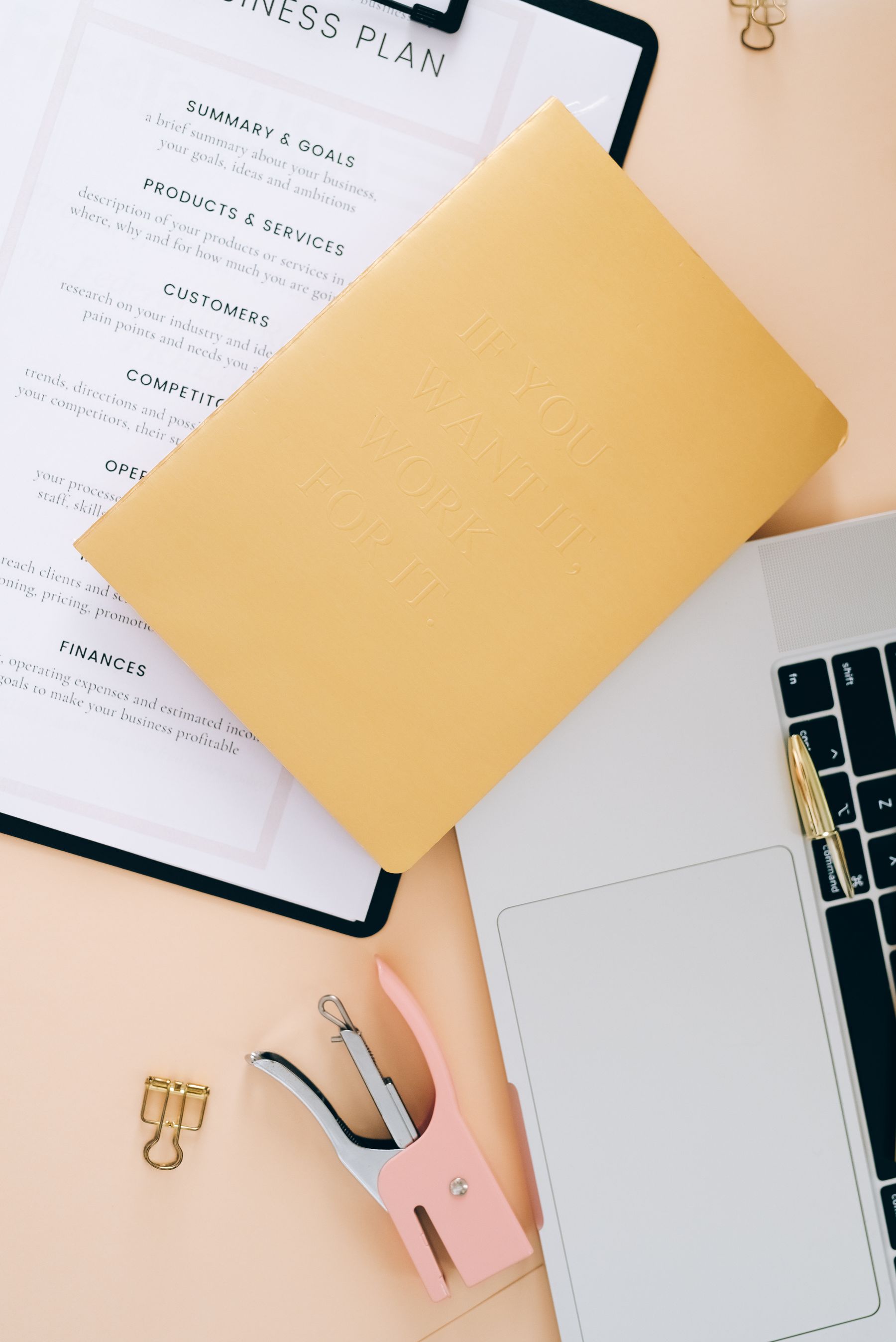 A laptop, planning document, and notebook arranged on a working desk.
